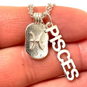 May include: Silver necklace with a Pisces zodiac sign charm and a separate charm with the word "Pisces" spelled out vertically.