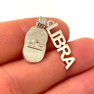 May include: Silver charm with a Libra zodiac symbol and the word "LIBRA" written vertically.
