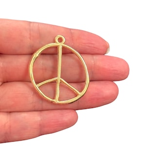 May include: A gold-coloured peace sign charm with a loop at the top for attaching to jewellery or other crafts. The peace symbol is a circle with a vertical line and two diagonal lines inside.