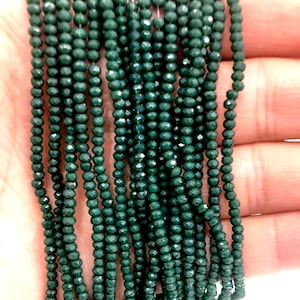 May include: A strand of dark green faceted glass beads. The beads are small and round, and they are strung on a clear thread.
