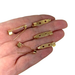 May include: Five gold-toned metal safety pin backs. The pins are all the same size and have a simple design.
