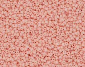May include: A close-up image of a large quantity of small, round, opaque pink beads. The beads are all the same size and shape, and they are arranged in a random pattern.