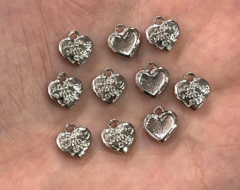 Puede incluir: Diez dijes de plata en forma de corazón con un diseño floral y las palabras "Forever Yours" grabadas en cada dije.