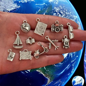 May include: A collection of silver charm pendants featuring travel-themed designs, including a globe, a passport, a camera, sunglasses, a sailboat, a book, a scooter, an airplane, a car, a suitcase, and a passport.