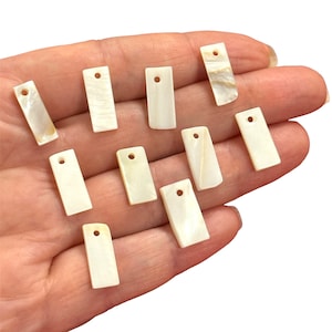 May include: A selection of rectangular, off-white mother-of-pearl pendants, each with a small hole for threading. The pendants display a natural, iridescent shimmer and unique patterns. These pendants are suitable for jewellery making.
