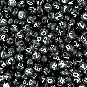 Peut inclure: Une image en gros plan d'une grande quantité de perles de lettres noires. Les perles sont rondes et portent des lettres blanches. Les lettres sont toutes différentes et disposées de manière aléatoire.