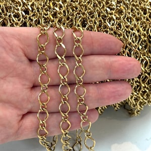 Könnte beinhalten: Eine durchgehende goldfarbene Metallkette mit länglichen, ovalen Gliedern, die durch kleinere kreisförmige Ringe verbunden sind. Die Kette hat eine polierte, reflektierende Oberfläche und ist als aufgewickeltes Bündel dargestellt.