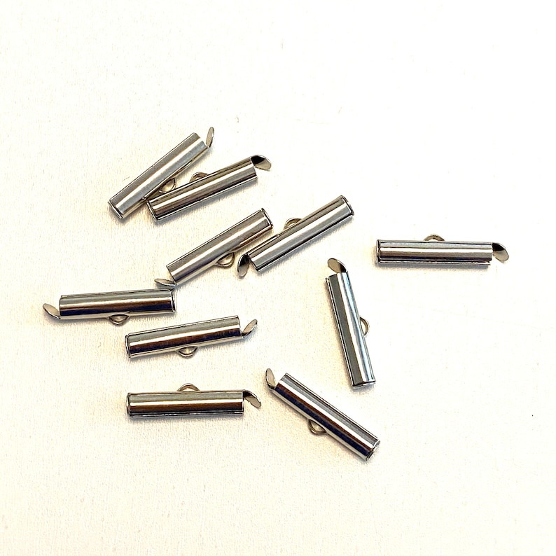 May include: A group of ten silver metal tube end caps for jewelry making. The end caps are about 1 inch long and have a small loop on one end.