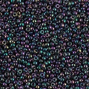 Op de afbeelding: Een close-up van een grote hoeveelheid kleine, ronde, iriserende kralen. De kralen zijn een mix van donkerblauw, paars en groen.