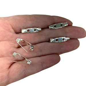 May include: Five silver-toned metal pin back closures for crafts and jewelry making. The pin backs are oval shaped with two holes on each side.