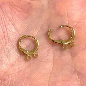 May include: Two gold-toned earring hoops with a hinged closure and three small jump rings hanging from the bottom.