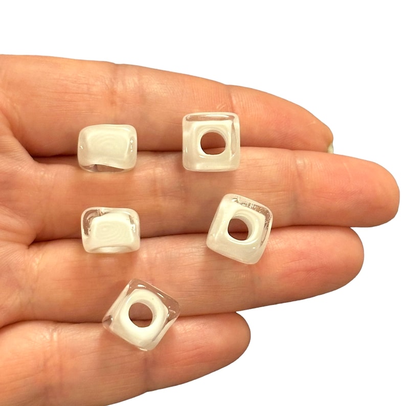 May include: Five white square beads with a hole in the center. The beads are translucent and have a slightly frosted appearance.
