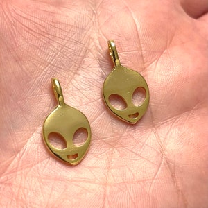 Puede incluir: Dos abalorios de cabeza de extraterrestre de color dorado con un diseño sencillo. Los abalorios son pequeños y tienen un agujero en la parte superior para sujetarlos a un collar o pulsera.