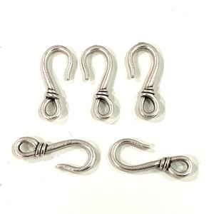 Puede incluir: Cinco ganchos de metal plateados con un lazo anudado en la parte superior. Los ganchos son todos del mismo tamaño y forma.