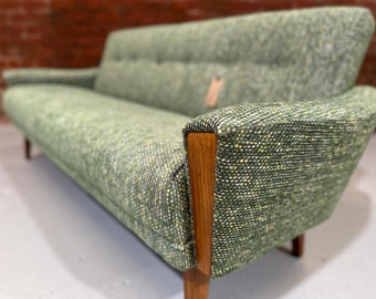 May include: A green patterned sofa with wooden arms and legs. The sofa has a tufted back and a simple, modern design.