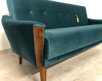 May include: Teal velvet sofa with wooden arm accents and legs. The sofa has a mid-century modern design with a button-tufted back. The wooden armrests have a unique angled design. The sofa is approximately 78 inches long.