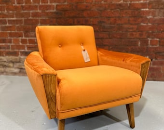 May include: A bright orange armchair with wooden legs and arms. The chair has a button tufting detail on the back and a small tag hanging from the back.