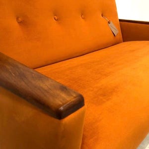 May include: A two-seater orange velvet sofa with wooden arms. The sofa has a tufted back and a simple design.