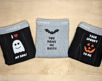 Op de afbeelding: Drie paar zwarte en grijze boxershorts met Halloween-thema's. Een paar heeft een spook met de tekst "Ik hou van mijn boo!" Een ander paar heeft een vleermuis met de tekst "Je maakt me gek!" Het laatste paar heeft een jack-o-lantern met de tekst "Praat met me over spookjes."