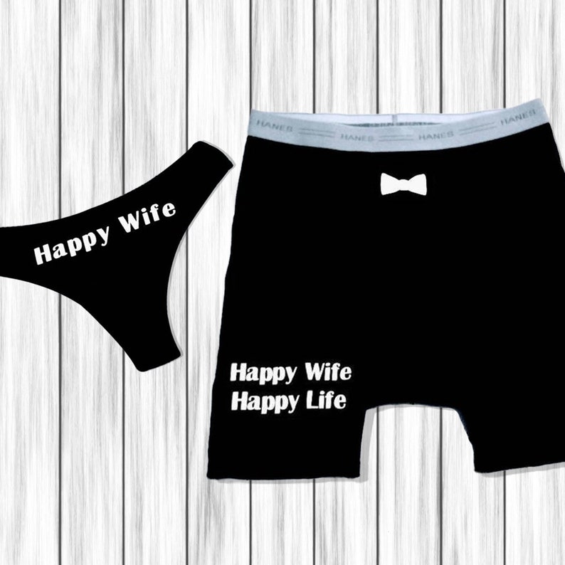以下が含まれることがあります： 黒い下着セット。「Happy Wife」の文字が入ったTバックと、「Happy Wife Happy Life」の文字が入ったボクサーパンツ。ボクサーパンツには白い蝶ネクタイのグラフィックが入っています。