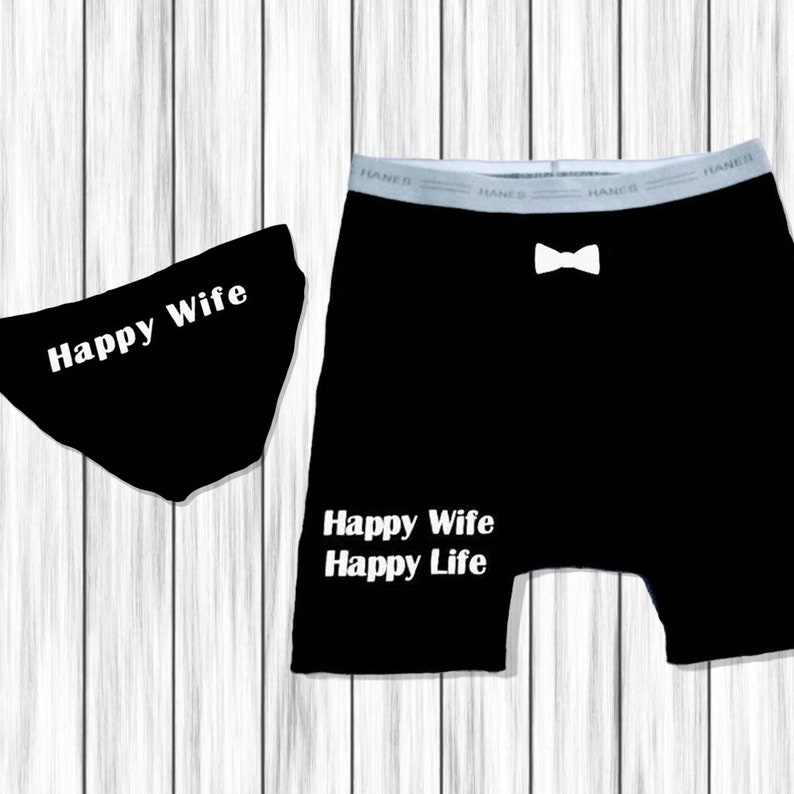 以下が含まれることがあります： 黒い下着セット。ブリーフには「Happy Wife」の文字、ボクサーパンツには白い蝶ネクタイのグラフィックと「Happy Wife Happy Life」の文字が入っています。