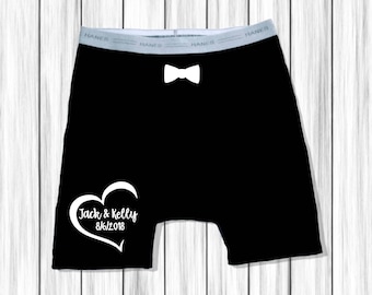 May include: Black boxer shorts with a white bow tie and a white heart with the text "Jack & Kelly 8/6/2018" on the left leg.