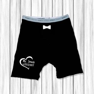 Op de afbeelding: Zwarte boxershorts met een witte vlinderdas en een wit hart met de tekst "Mr. Jones 6/15/2007" gedrukt op de voorkant.