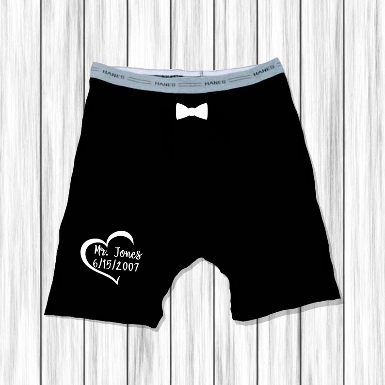 Op de afbeelding: Zwarte boxershorts met een witte vlinderdas en een wit hart met de tekst "Mr. Jones 6/15/2007" gedrukt op de voorkant.