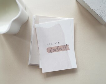 Puede incluir: Una pila de tarjetas blancas con un diseño de acuarela y el texto alemán "ICH BIN WERTVOLL" en una fuente manuscrita. Las tarjetas tienen una paleta de colores suaves y neutros con un toque de marrón. Las tarjetas están apiladas sobre una superficie clara.