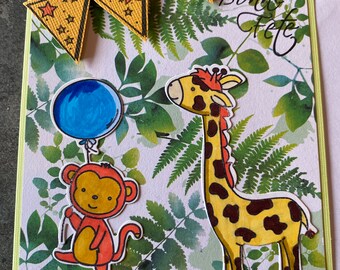 Pode incluir: Um cartão verde e branco com uma girafa, um macaco e um balão azul. O cartão tem uma faixa amarela com estrelas vermelhas e o texto "Bonne Fete".