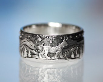 Puede incluir: Un anillo de plata con un diseño detallado de un lobo aullando a la luna en un entorno de bosque. El anillo está grabado con estrellas y árboles.