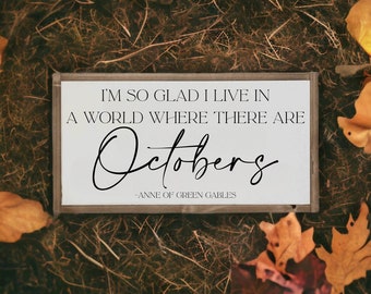 May include: A white wooden sign with black text that reads "I'm so glad I live in a world where there are Octobers - Anne of Green Gables". The sign is surrounded by brown and orange leaves.
