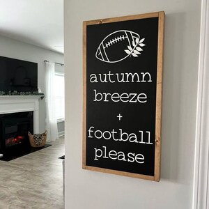 K&ouml;nnte beinhalten: Schwarz-wei&szlig;es Schild mit Holzrahmen. Das Schild sagt "autumn breeze + football please" mit einer wei&szlig;en Fu&szlig;ball- und Bl&auml;ttergrafik.