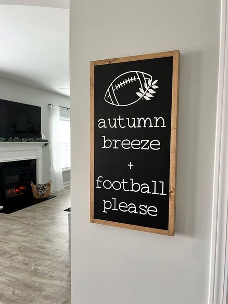 K&ouml;nnte beinhalten: Schwarz-wei&szlig;es Schild mit Holzrahmen. Das Schild sagt "autumn breeze + football please" mit einer wei&szlig;en Fu&szlig;ball- und Bl&auml;ttergrafik.