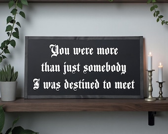 May include: A framed black sign with white gothic lettering that reads, "You were more than just somebody I was destined to meet." The sign is on a wooden shelf with candles and plants.