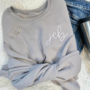 May include: A gray sweatshirt with the name "jcb" embroidered in white on the front.