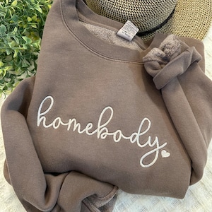 Peut inclure: Un sweat-shirt marron avec le mot "homebody" brod&eacute; en blanc avec un petit c&oelig;ur &agrave; c&ocirc;t&eacute;.