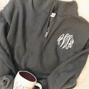 May include: Dark gray quarter-zip sweatshirt with a white monogram on the chest. A white mug with the words "SWEATER WEATHER" is visible. The mug has a dark red interior.