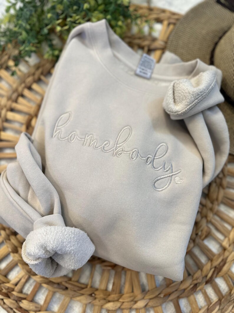 Peut inclure: Un sweat-shirt beige clair avec le mot "homebody" brod&eacute; en blanc sur le devant.