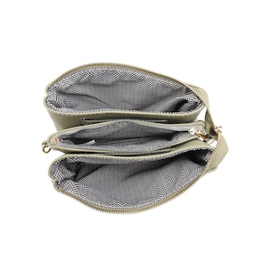 Puede incluir: Un bolso bandolera de color verde claro con tres compartimentos separados con cremallera. El bolso est&aacute; abierto y el forro es de un patr&oacute;n de espiga en blanco y negro.