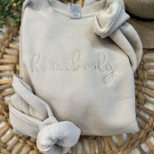 Peut inclure: Un sweat-shirt gris clair avec le mot "homebody" brod&eacute; en blanc sur le devant.