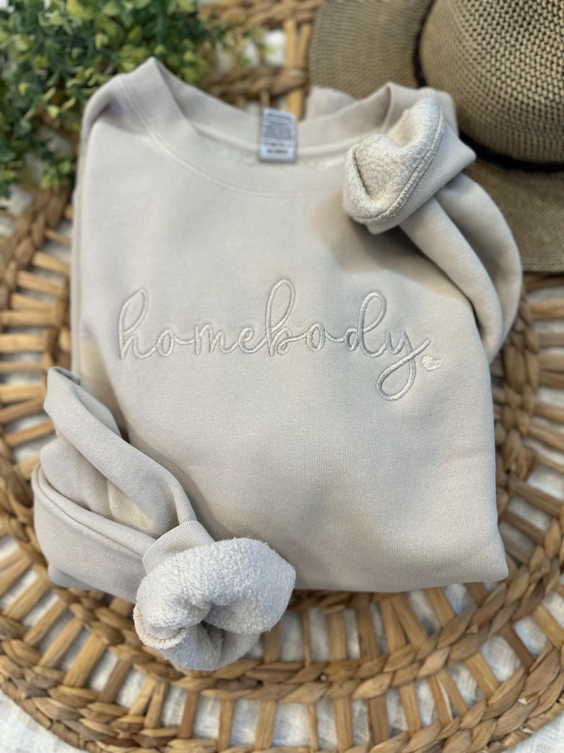 Peut inclure: Un sweat-shirt gris clair avec le mot "homebody" brod&eacute; en blanc sur le devant.