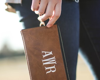 May include: A brown leather clutch with a zipper and a white embroidered monogram that says "AWMR".
