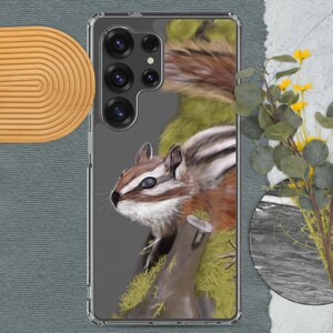 May include: Clear phone case featuring a detailed illustration of a chipmunk. The chipmunk has brown, white, and black markings, set against a gray background. The case also includes a tree trunk with green moss and a sprig of yellow flowers.