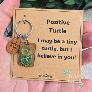 Può includere: Un portachiavi Positive Turtle con un ciondolo a forma di tartaruga in vetro e un'etichetta di legno con la scritta "I believe in you". La carta recita "I may be a tiny turtle, but I believe in you!" e presenta il marchio "Purus Sensa".