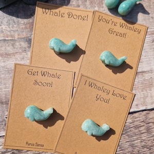 May include: Five brown cards with whale-shaped green stones on them. The cards have different messages on them, including "Whale Done!" and "Get Whale Soon!"