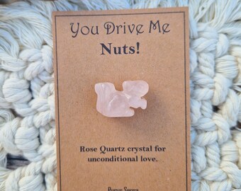 May include: A card with the text "You Drive Me Nuts!" and a pink rose quartz crystal. The card also says "Rose Quartz crystal for unconditional love." and "Purus Sensa".
