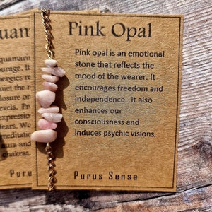 May include: Pink Opal crystal bracelet with gold chain and a brown card with the text "Pink Opal" and information about the stone's properties. The card also includes the text "Purus Sensa".
