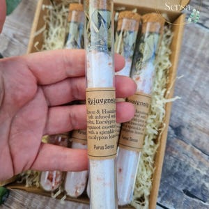 Pu&ograve; includere: Sei provette di vetro riempite con sali da bagno bianchi e foglie di eucalipto. Le provette sono etichettate "Rejuvenate" e "Purus Sensa".