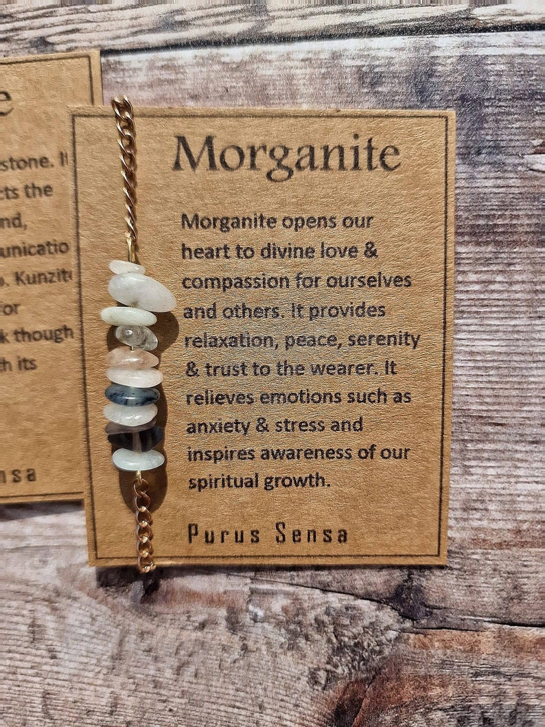 May include: A brown card with the text "Morganite" in large letters. The card describes the properties of the Morganite gemstone, including its ability to open the heart to divine love, provide compassion, and promote relaxation, peace, and serenity. The card also mentions that Morganite relieves emotions such as anxiety and stress and inspires awareness of spiritual growth. The text "Purus Sensa" is printed at the bottom of the card.